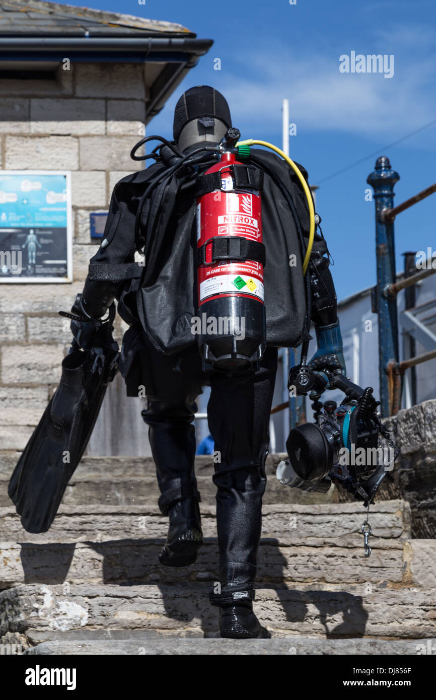 Diver in wet suit and holding flippers & diving mask climbing steps at Swanage Pier, Dorset Stock Photo