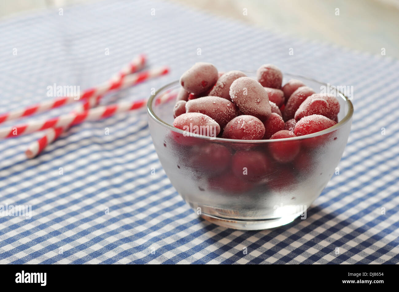 Frozen cornel berries in glass bowl and striped straws on checkered background Stock Photo