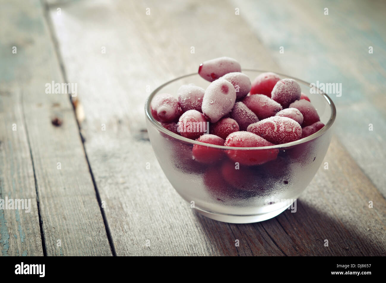 Frozen cornel berries in glass bowl and on wooden background Stock Photo