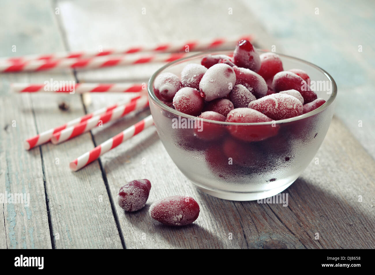Frozen cornel berries in glass bowl and striped straws on wooden background Stock Photo