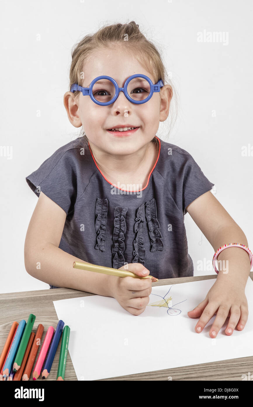 Blond cute little girl with blue glasses painting on a school desk in