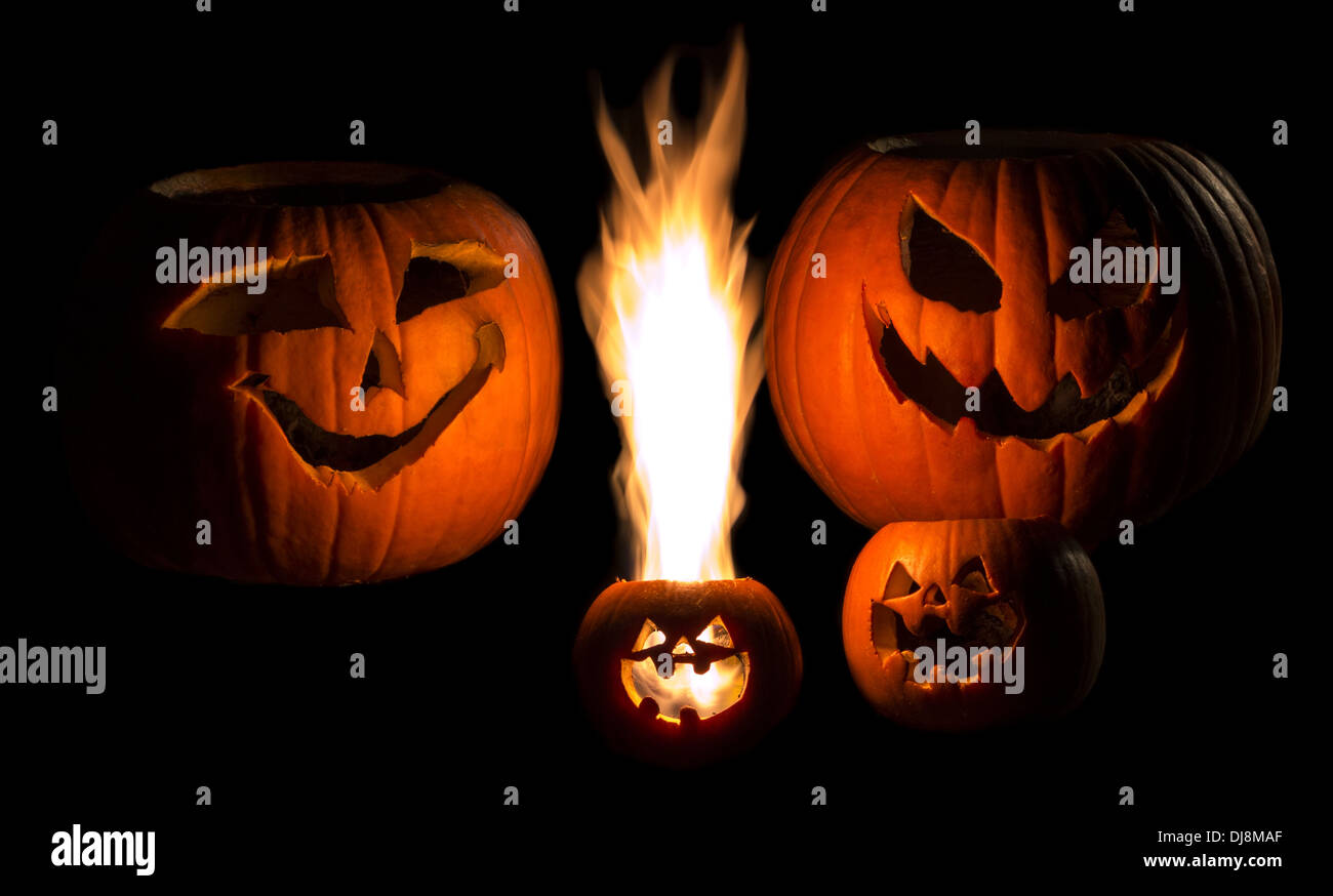 A family of jack-o-lanterns isolated on black. The youngest child has a large yellow flame coming out of his head. Stock Photo