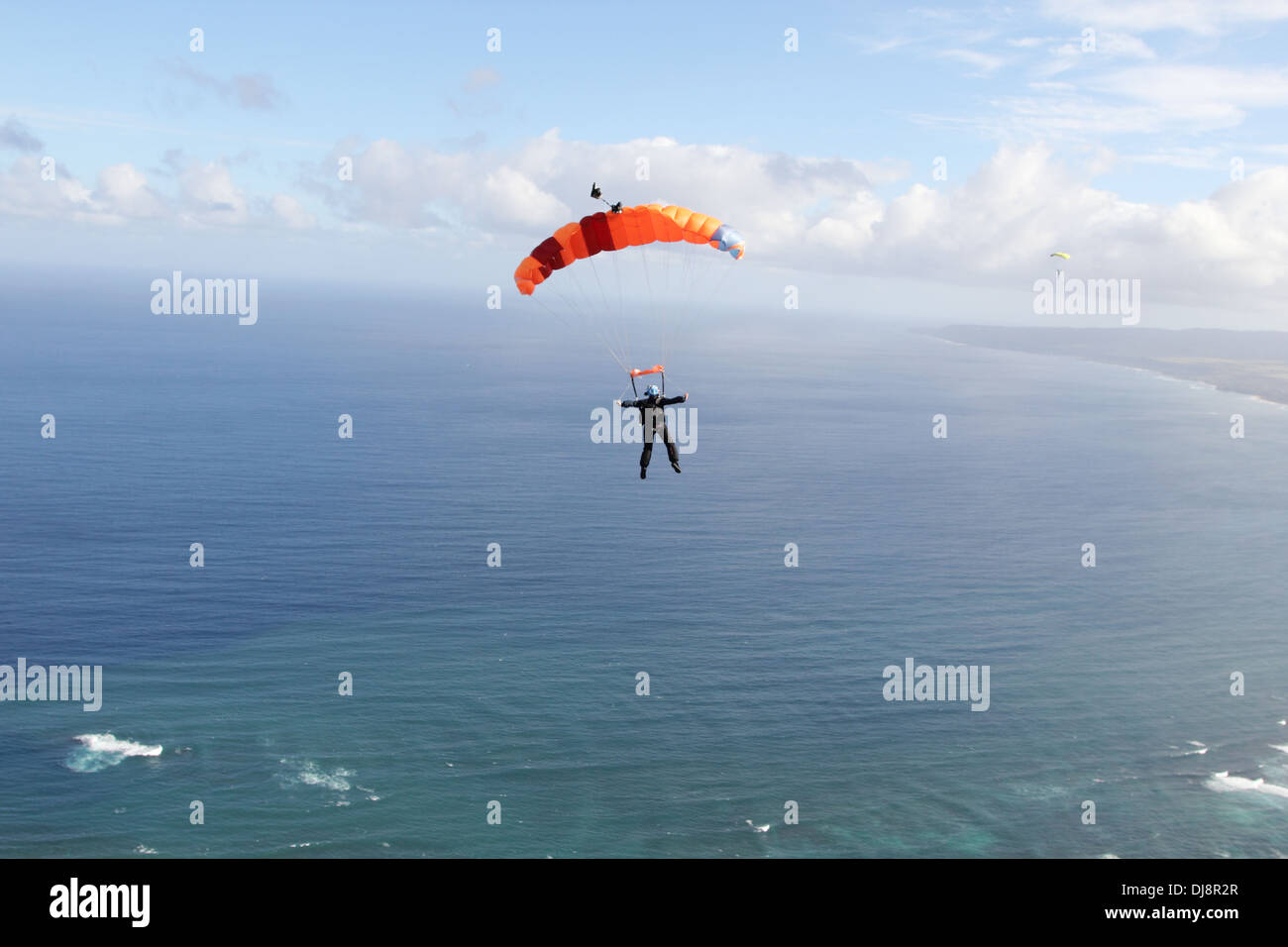 Skydiver under canopy is flying high in the sky over clouds into direction open sea. She is looking for a suitable landing area! Stock Photo