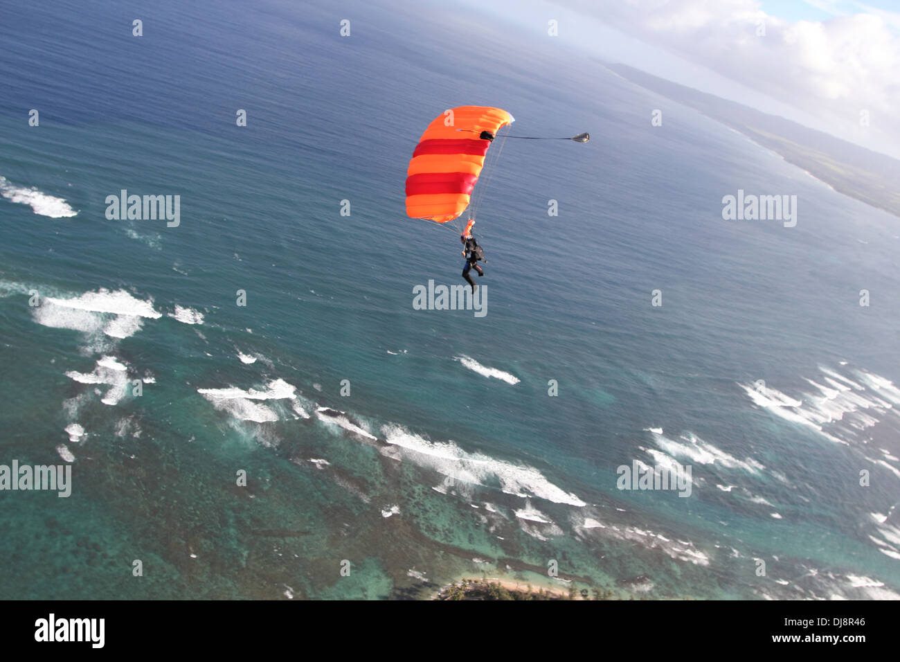 Skydiver under canopy is flying high in the sky over clouds into direction shore line. Soon she will land save on the beach. Stock Photo