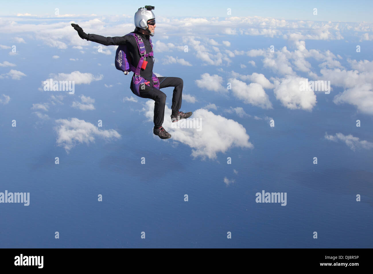 This skydiver has a video camera mounted on his helmet and is filming another jumper in the sky over clouds. Stock Photo
