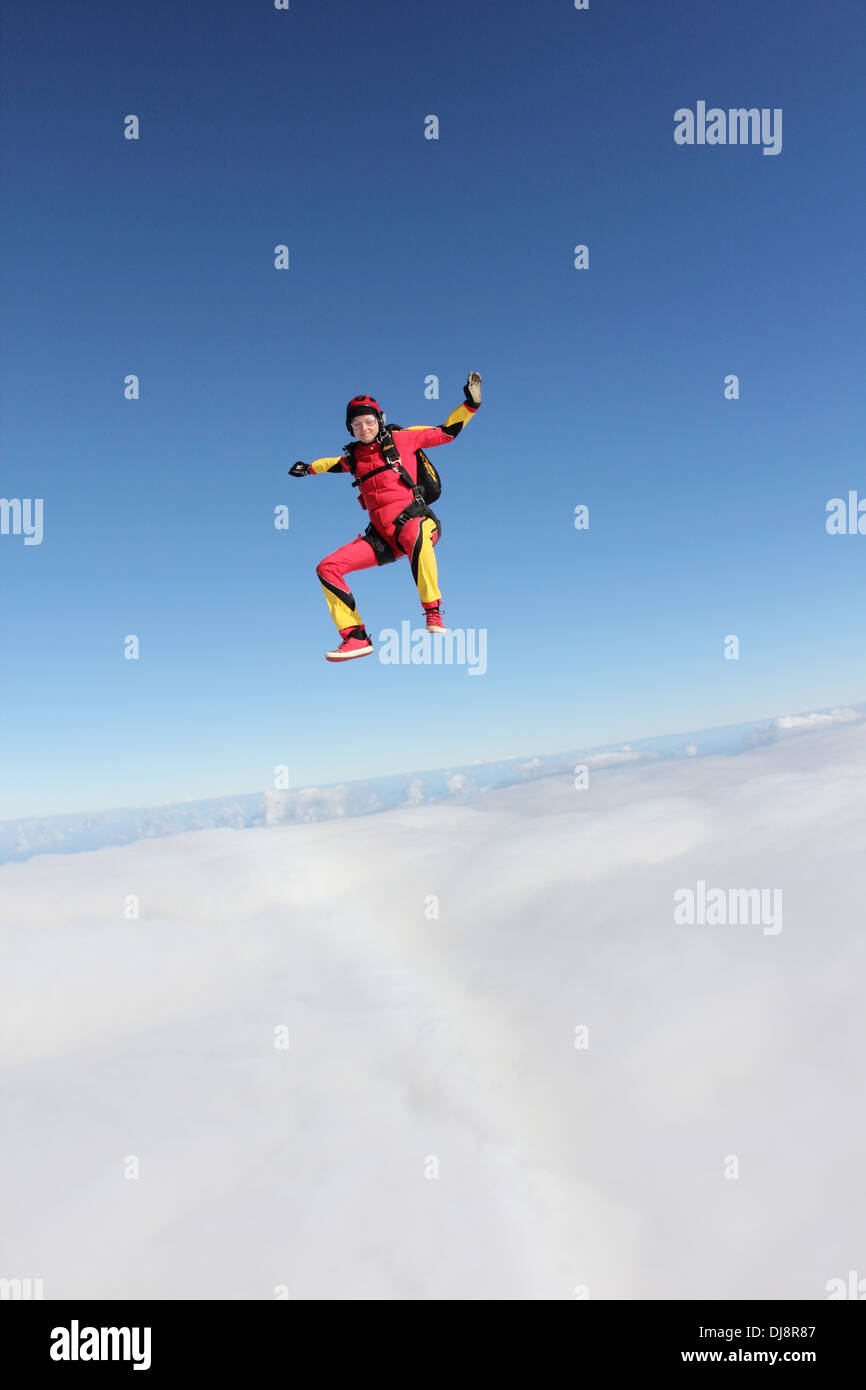 This skydiver woman is falling free in a sit position over a big cloud. She is smiling and having fun in the blue sky. Stock Photo