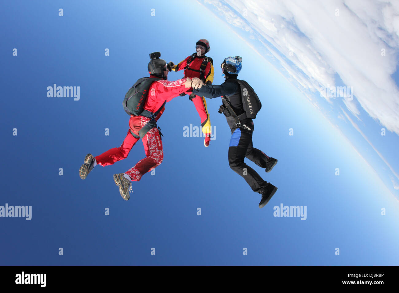 This skydiver team is flying head over in the blue sky. They hold hand and form a star formation together over clouds. Stock Photo