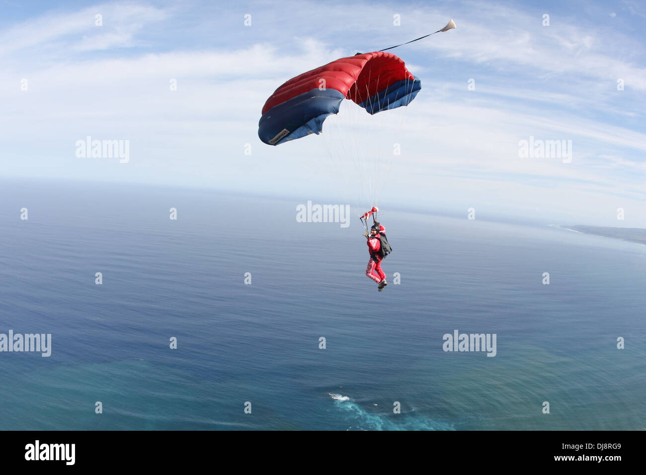 Skydiver under canopy is flying high in the sky over clouds into direction open sea. He is looking for a suitable landing area! Stock Photo