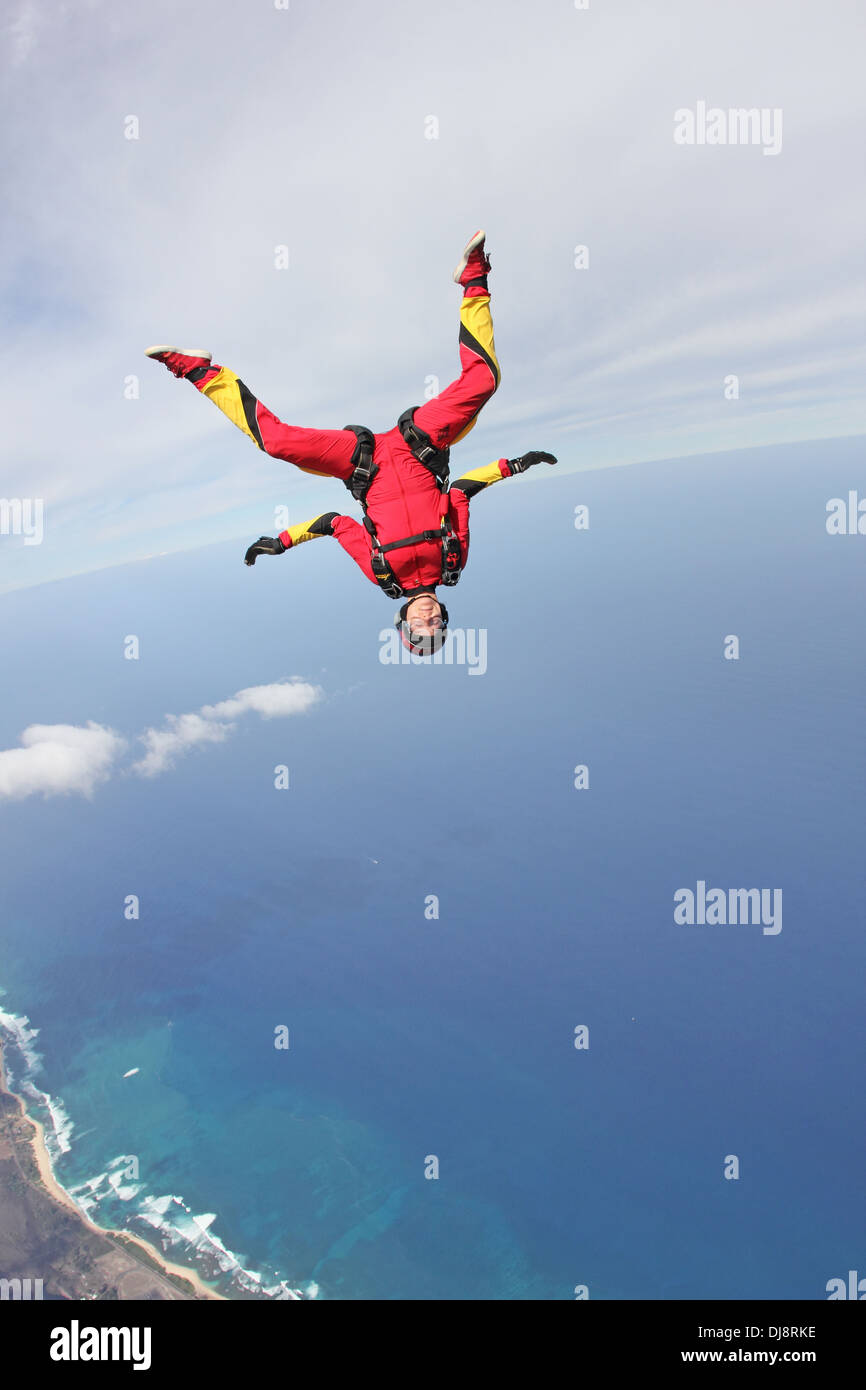 This skydiver girl is flying in a head down position over the deep blue sea next to the shore line with high speed of 130 MPH. Stock Photo