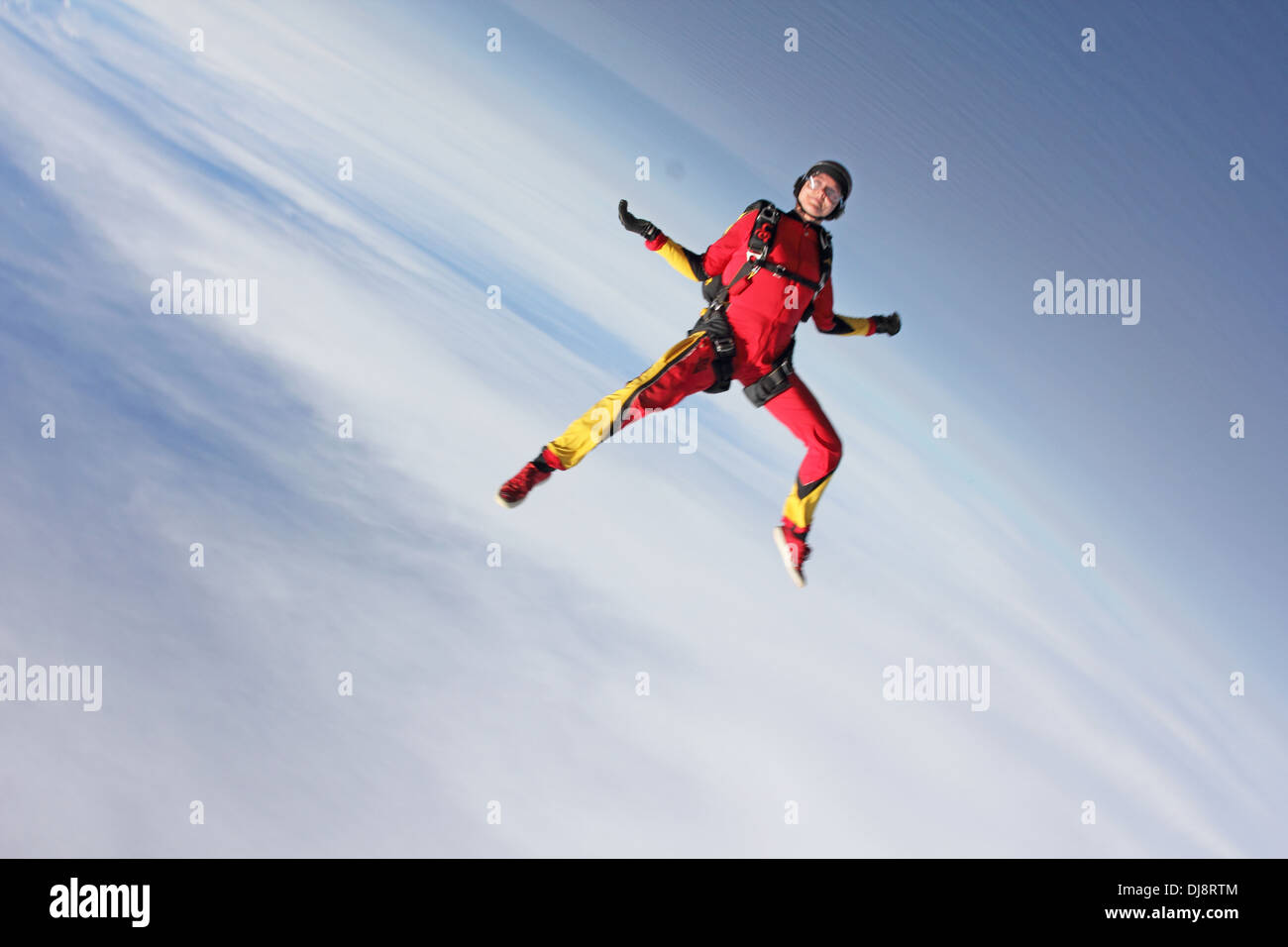 This skydiver woman is falling free in a head down position over the blue sky. She is tracking downwards with over 130 MPH. Stock Photo