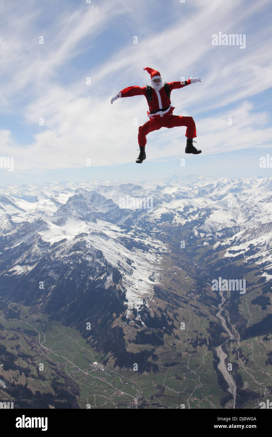 This skydiver in a Santa Claus costume is falling free in a sit position over a white mountain area with over 120 mph. Stock Photo