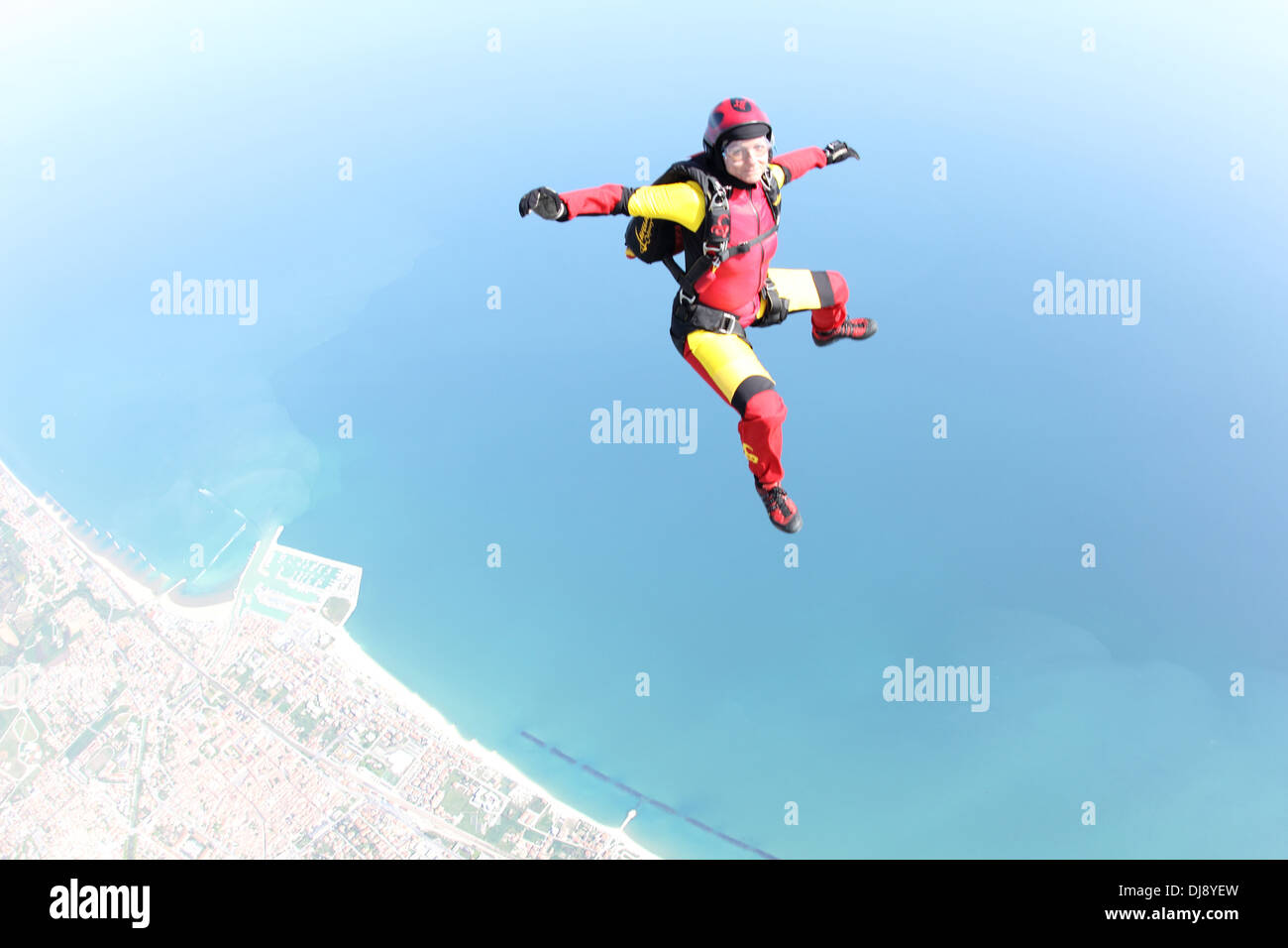 This skydiver woman is falling free in a sit position over a beautiful shore line. Thereby she has fun doing her sky-sport. Stock Photo