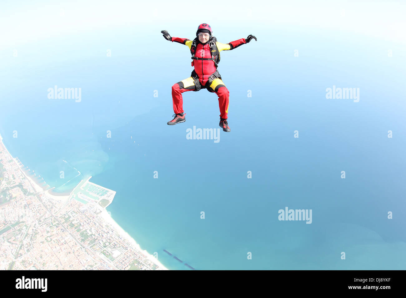 This skydiver woman is falling free in a sit position over a beautiful shore line. Thereby she has fun doing her sky-sport. Stock Photo
