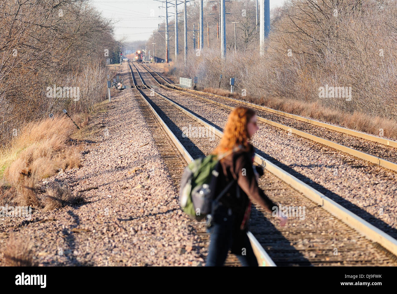 Woman crossing train tracks with approaching train. Stock Photo