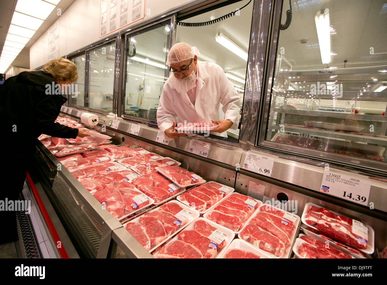 Hispanic employee wearing food safety hair net stocks with fresh meat department at a newly open COSTCO warehouse retail store Stock Photo