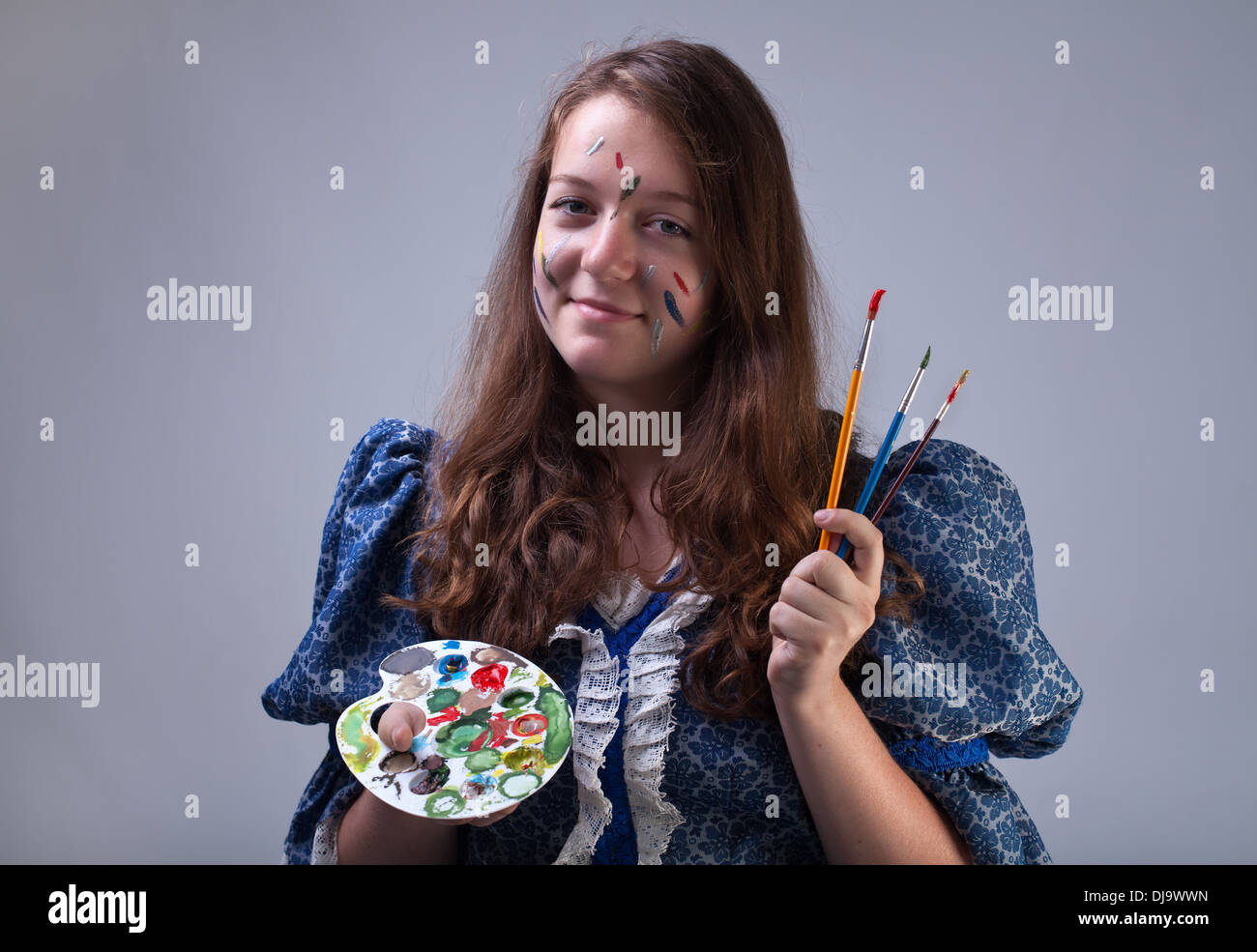 Young painter with smeary face holding palette and paintbrushes Stock Photo