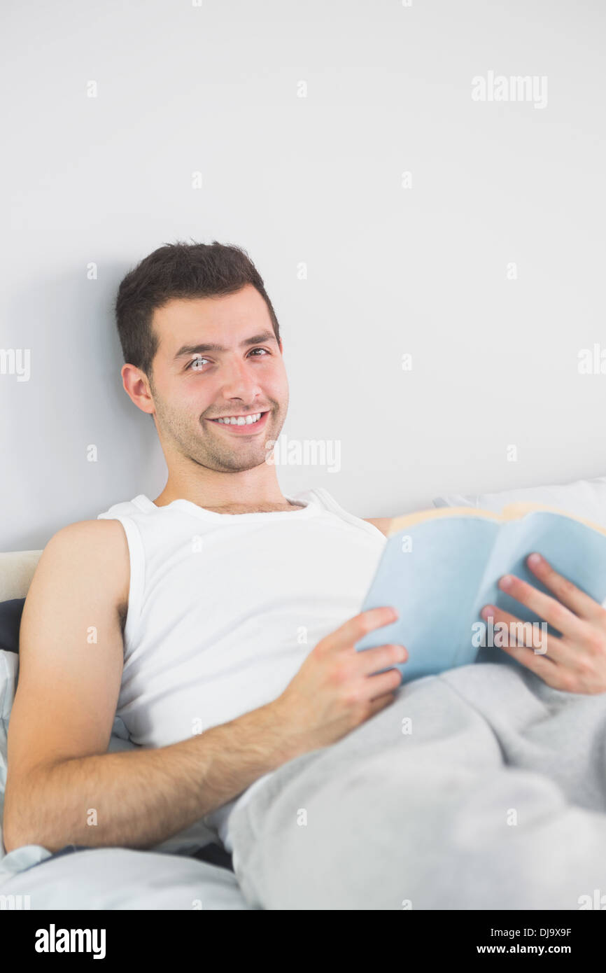 Handsome smiling man reading book in his bed Stock Photo