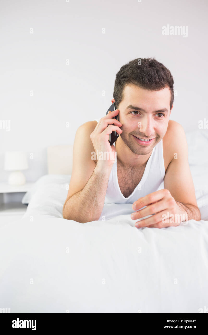 Smiling handsome man lying in bed phoning Stock Photo