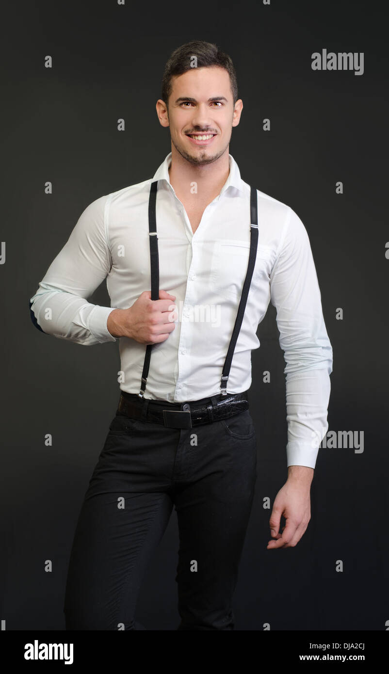 Elegant young man with white shirt and suspenders, on dark background, smiling, Stock Photo