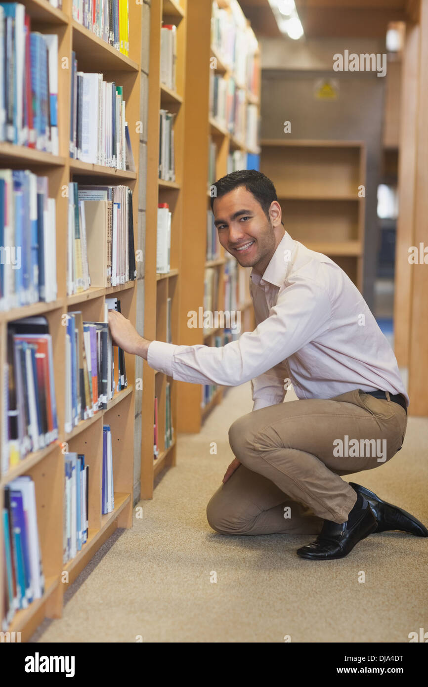 Young attractive man cowering in front of bookshelves Stock Photo