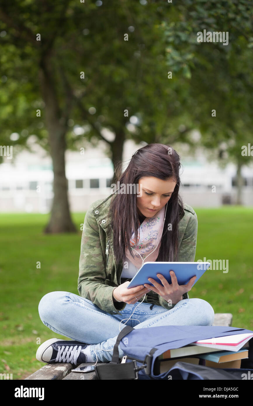 Focused brunette student using tablet sitting on bench Stock Photo