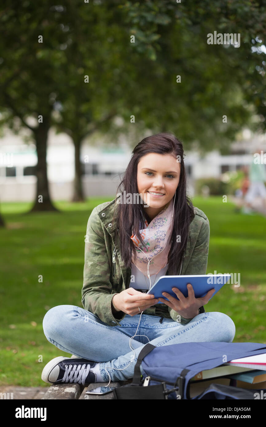 Smiling brunette student using tablet sitting on bench Stock Photo