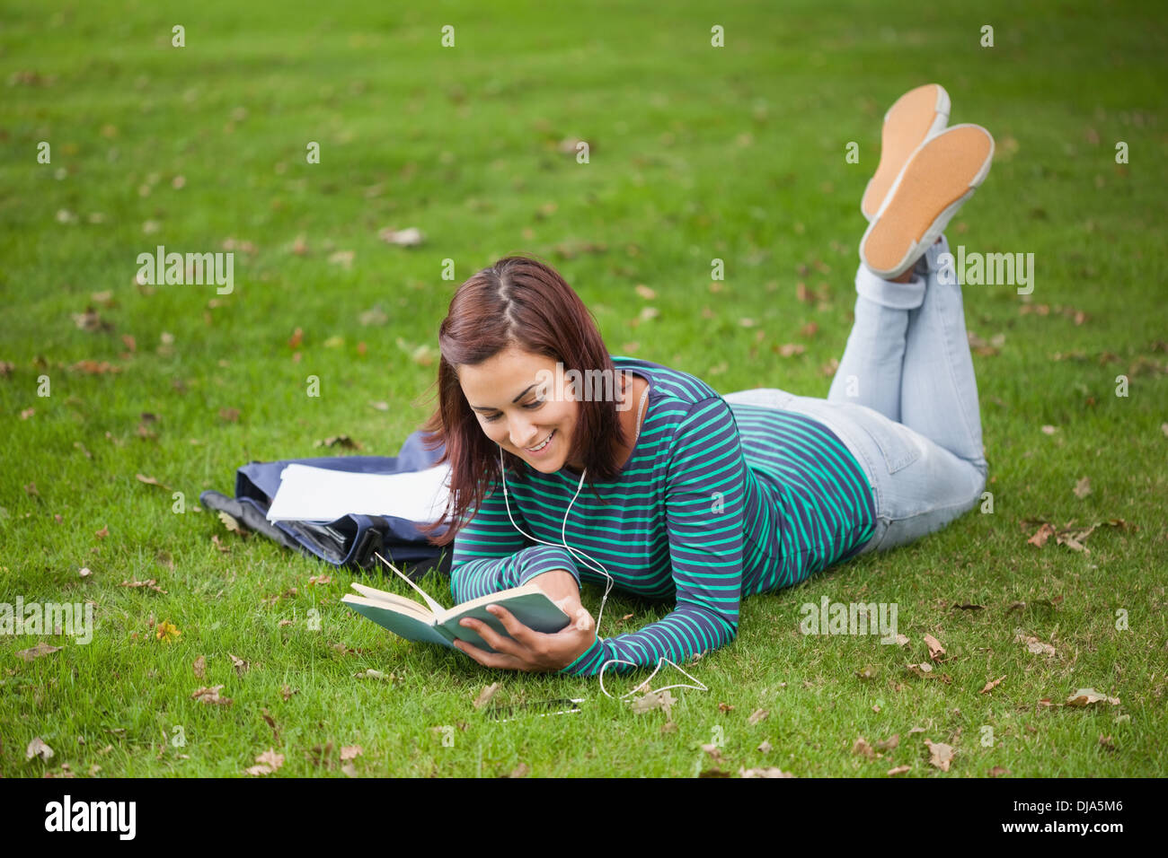 Happy casual student lying on grass reading Stock Photo