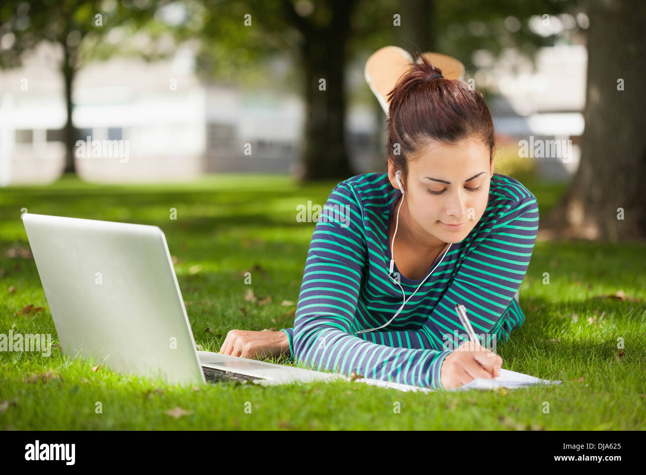 Calm casual student lying on grass taking notes Stock Photo