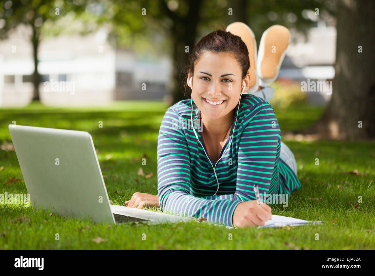 Happy casual student lying on grass taking notes Stock Photo