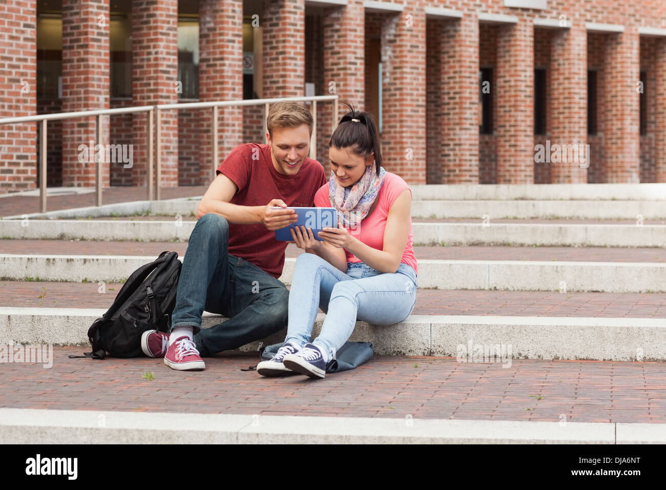 Happy students sitting on stairs using tablet Stock Photo