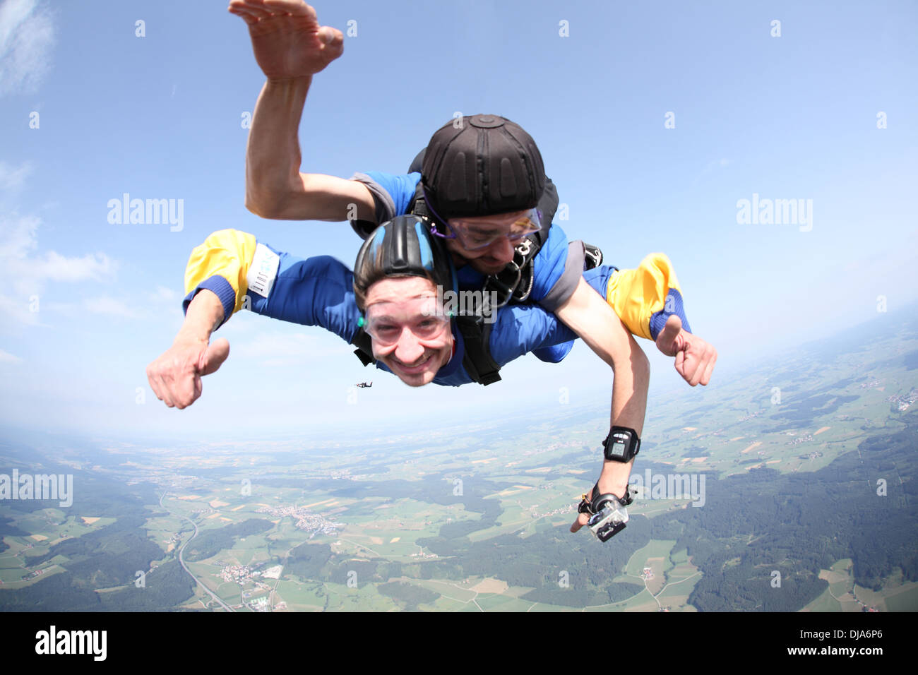 Tandem skydiver couple are having fun together in the sky. The passenger is smiling and the jump master checking the altitude. Stock Photo
