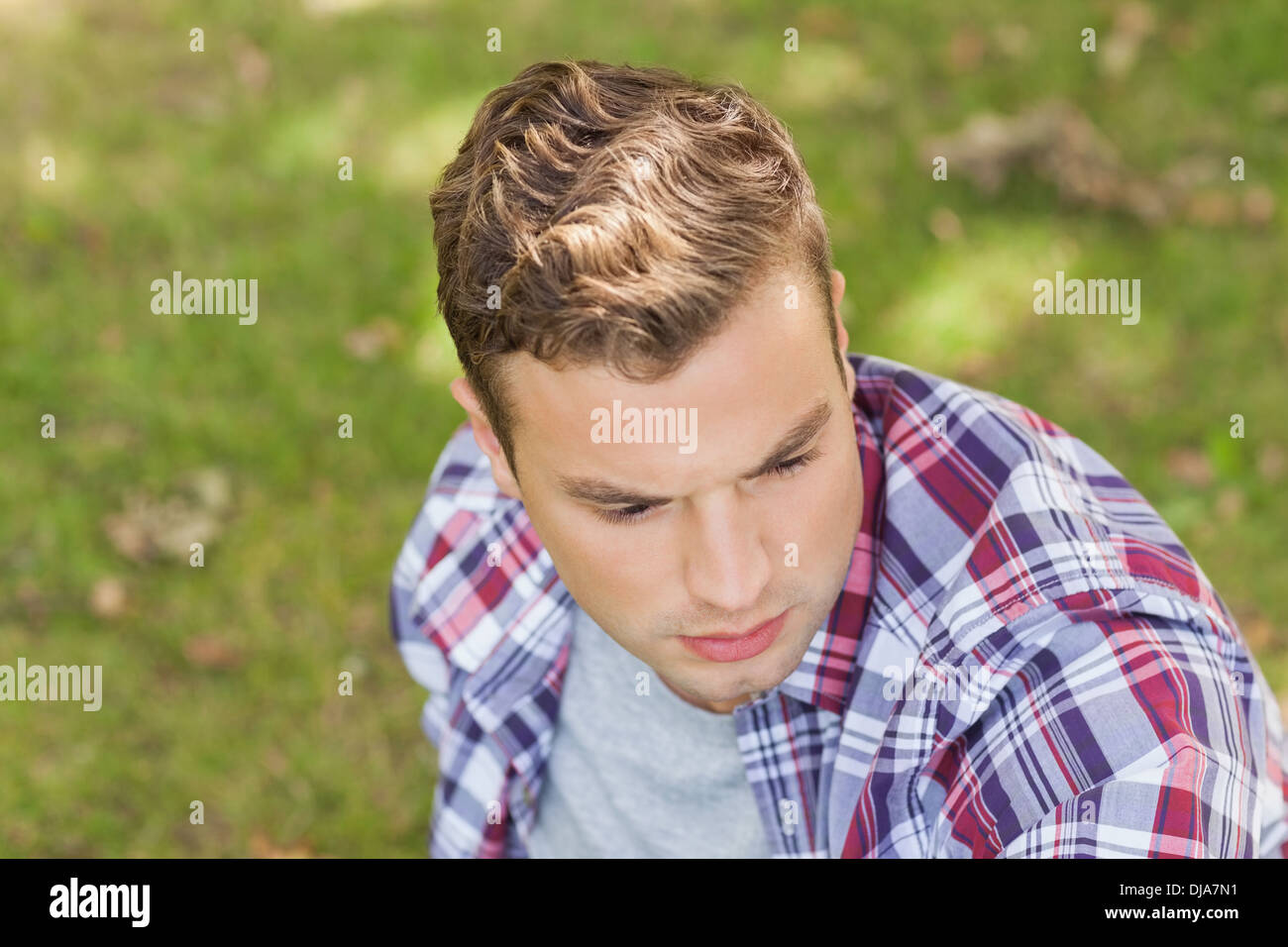 Handsome serious student sitting on grass Stock Photo