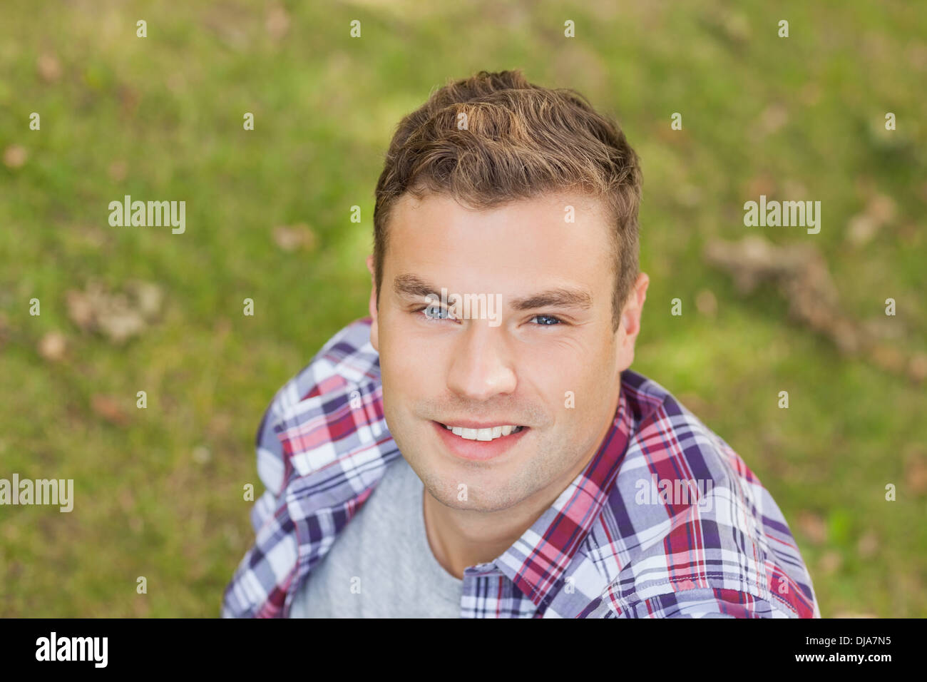 Handsome smiling student sitting on grass Stock Photo