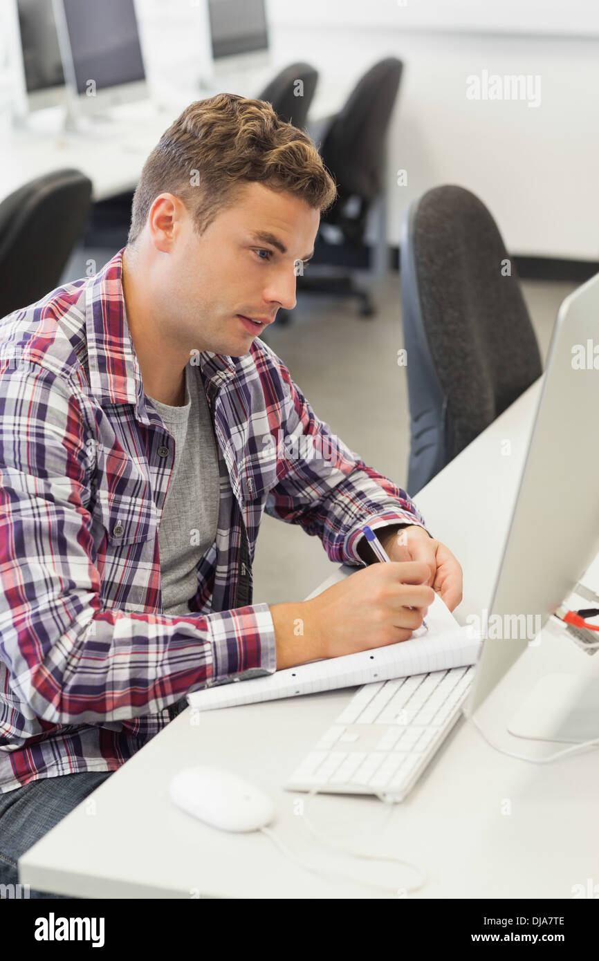 Handsome smiling student using computer taking notes Stock Photo