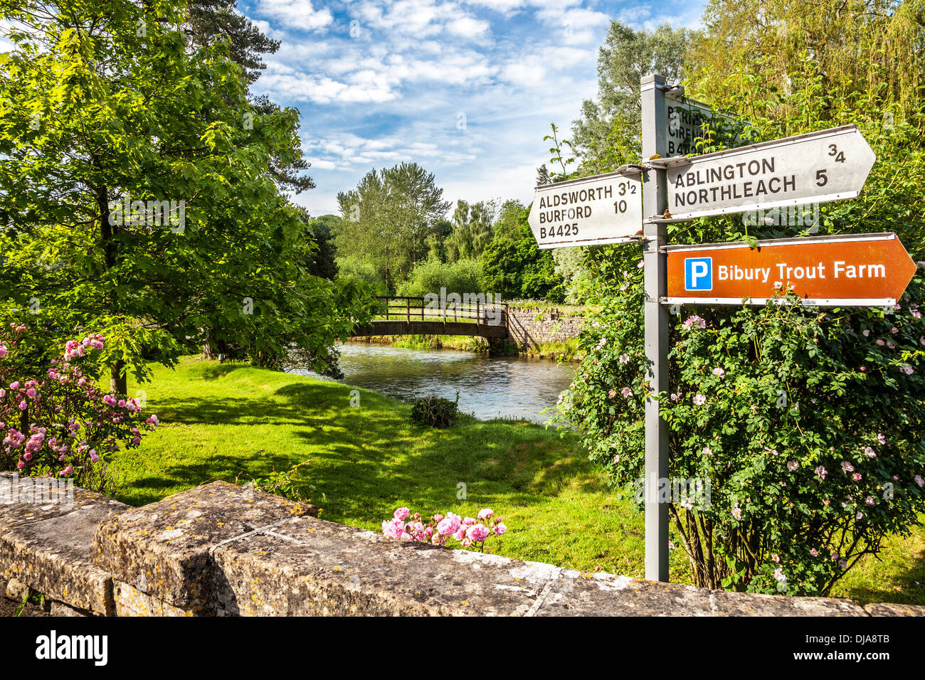 View over the River Coln in Bibury with a road sign to other Cotswold towns and villages and the Trout Farm. Stock Photo