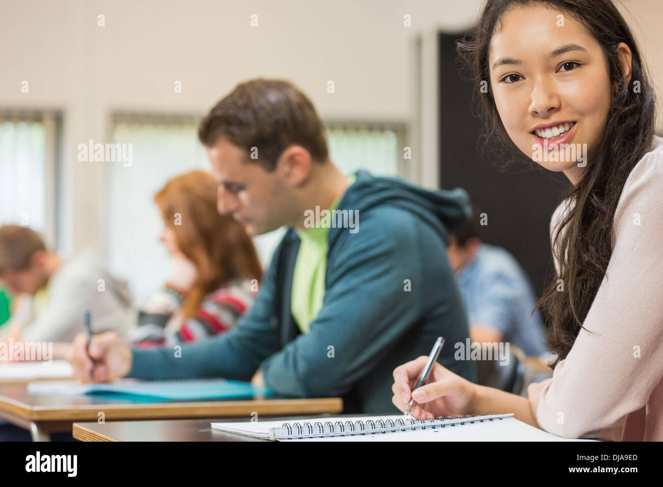 Female student with others writing notes in classroom Stock Photo