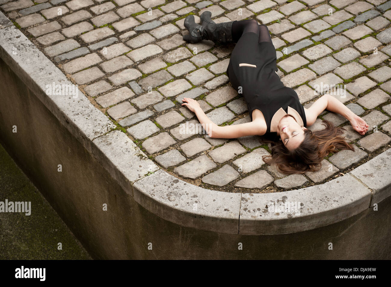 Elevated view of a woman wearing a black dress and lying down (dead?) on a cobbled road. Stock Photo