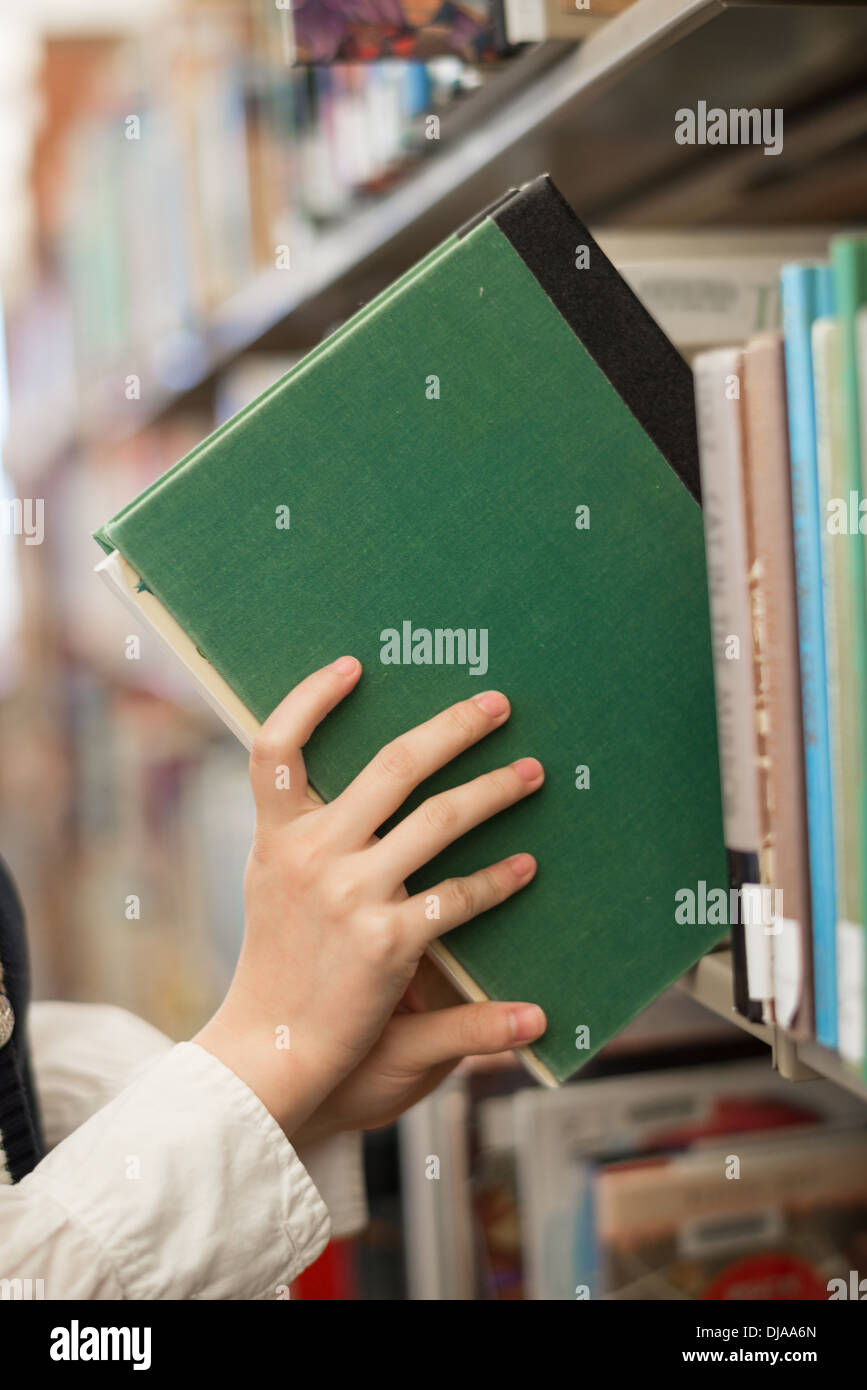 Student putting a green book back onto a bookshelf in library Stock