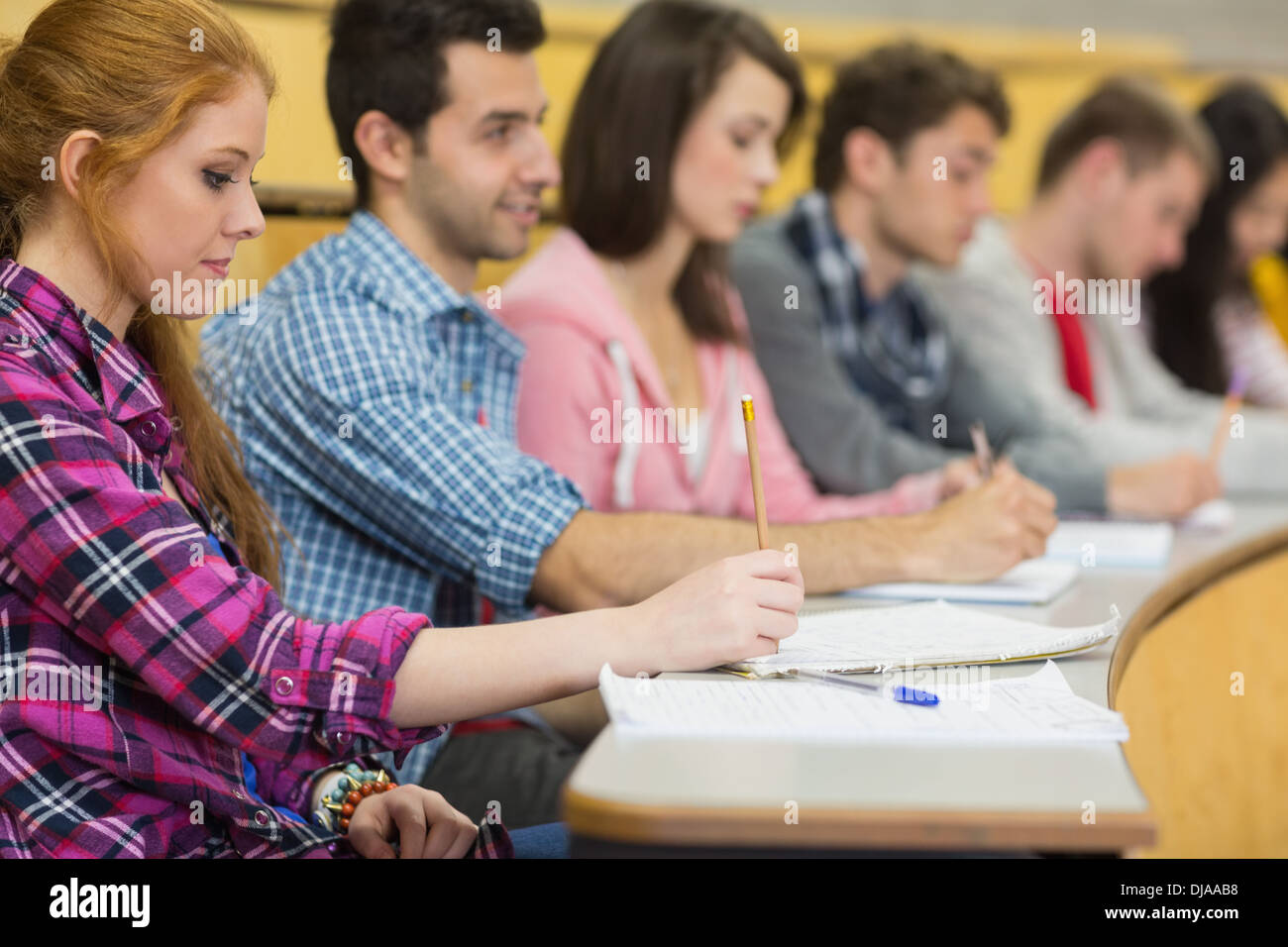 Students writing notes in a row at lecture hall Stock Photo