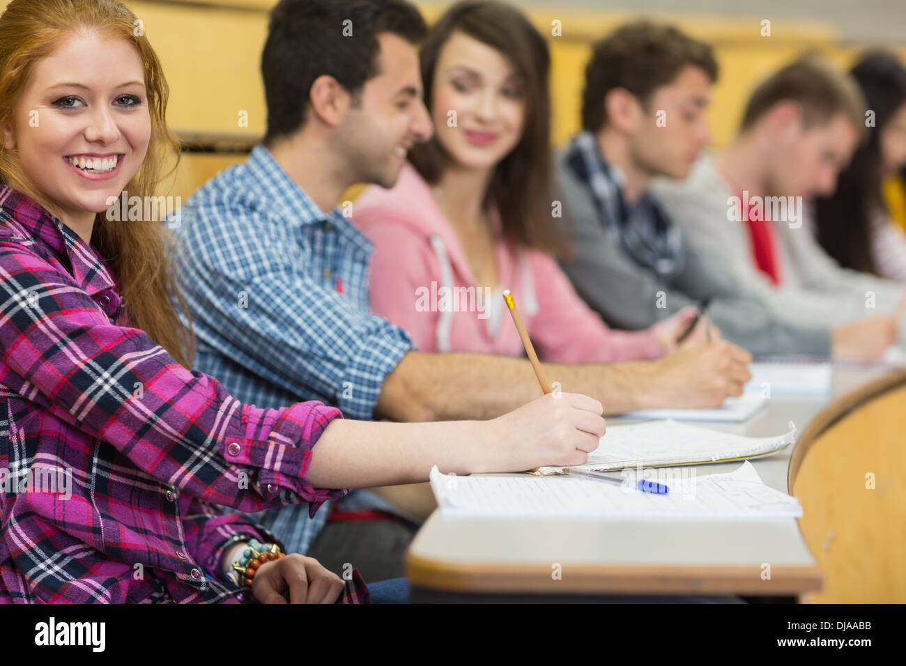 Smiling female with other students writing notes at lecture hall Stock Photo