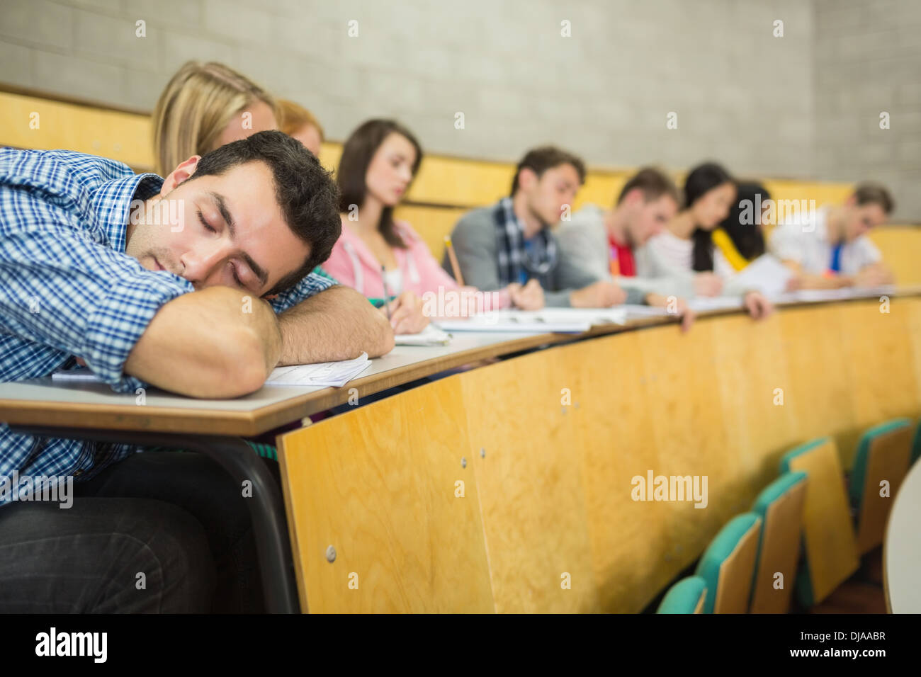 Male sleeping with students in lecture hall Stock Photo