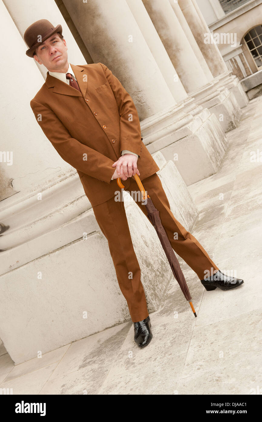 Slanted view of a snazzy dresser wearing a brown suit with a bowler hat and umbrella. Stock Photo