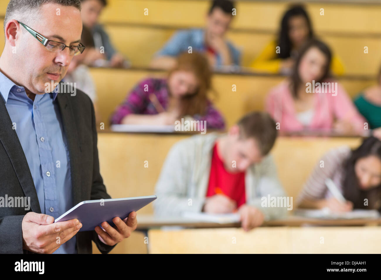 Teacher using tablet PC with students at lecture hall Stock Photo