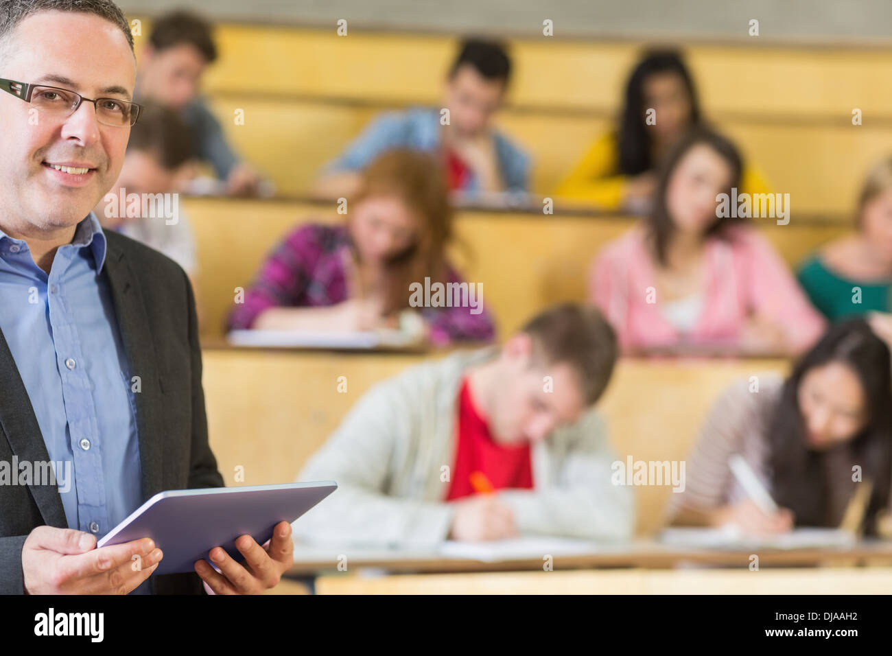 Teacher using tablet PC with students sitting at lecture hall Stock Photo