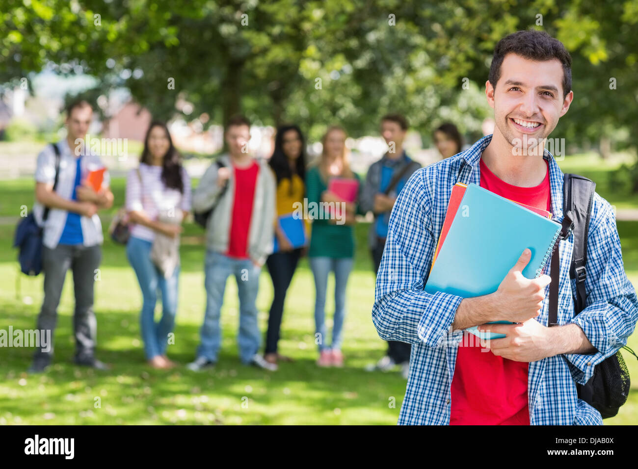 College boy holding books with blurred students in park Stock Photo