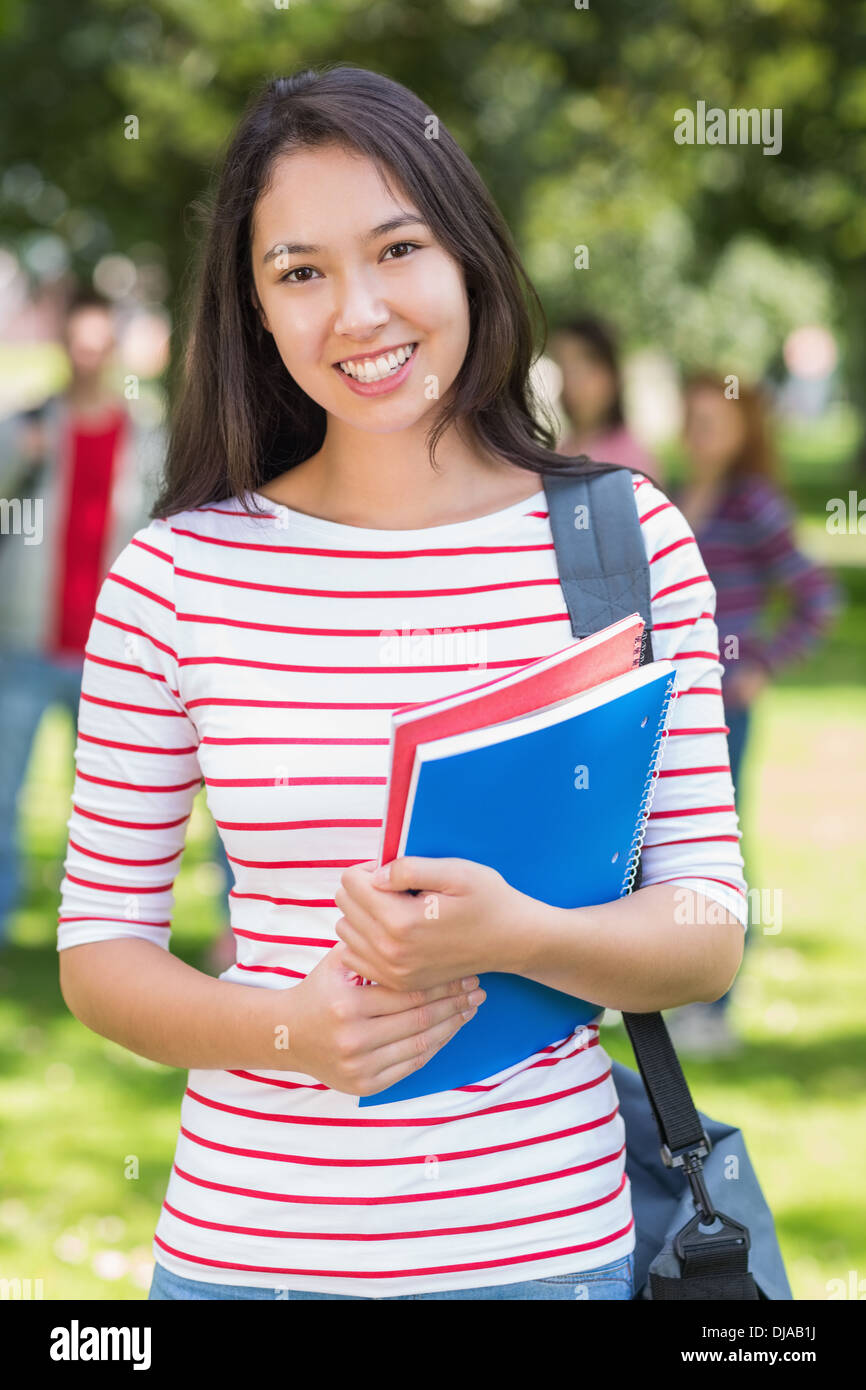College girl holding books with blurred students in park Stock Photo ...