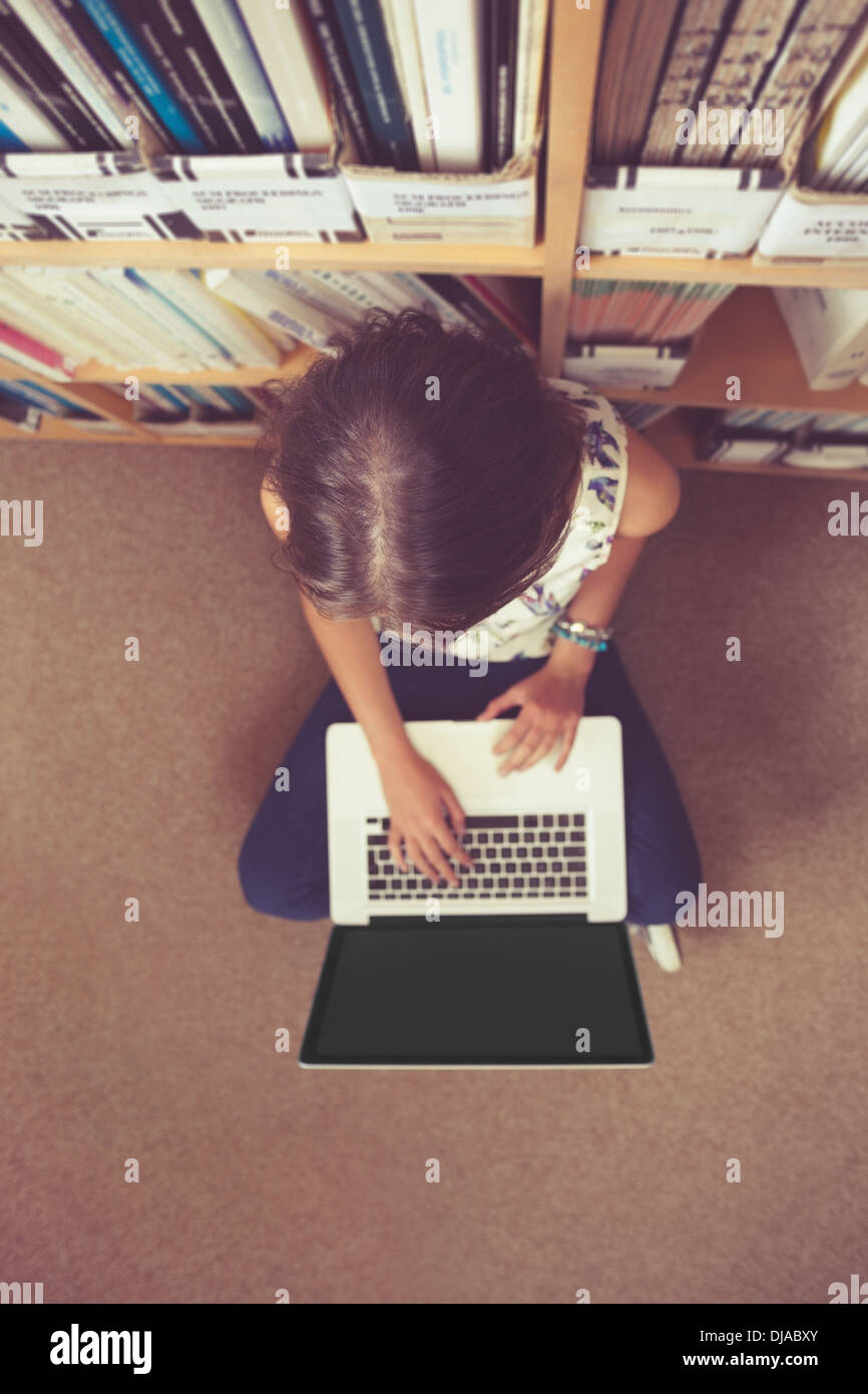 Student against bookshelf using laptop on the library floor Stock Photo ...