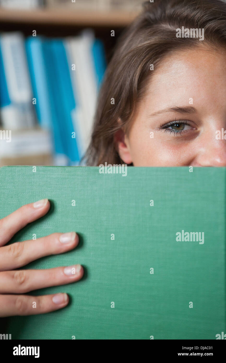 Female student holding book in front of her face in library Stock Photo ...
