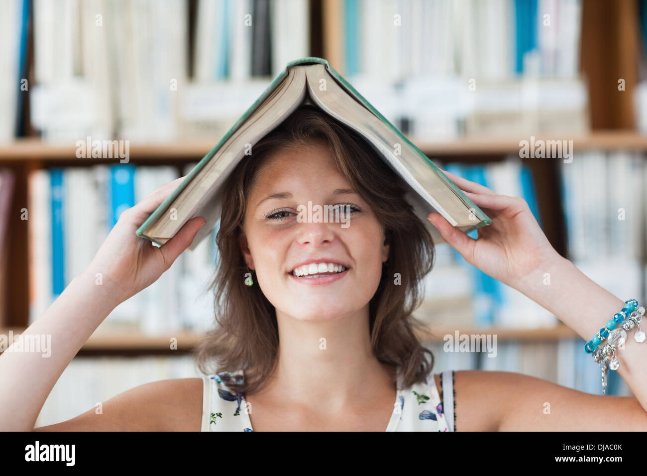 Female student holding book over her head in library Stock Photo - Alamy