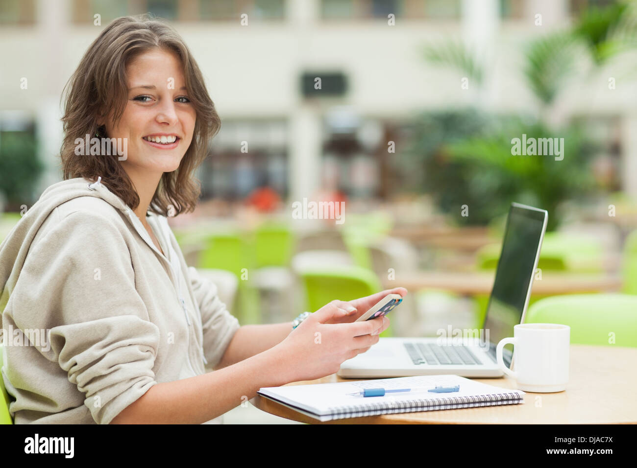 Student using cellphone and laptop at cafeteria table Stock Photo